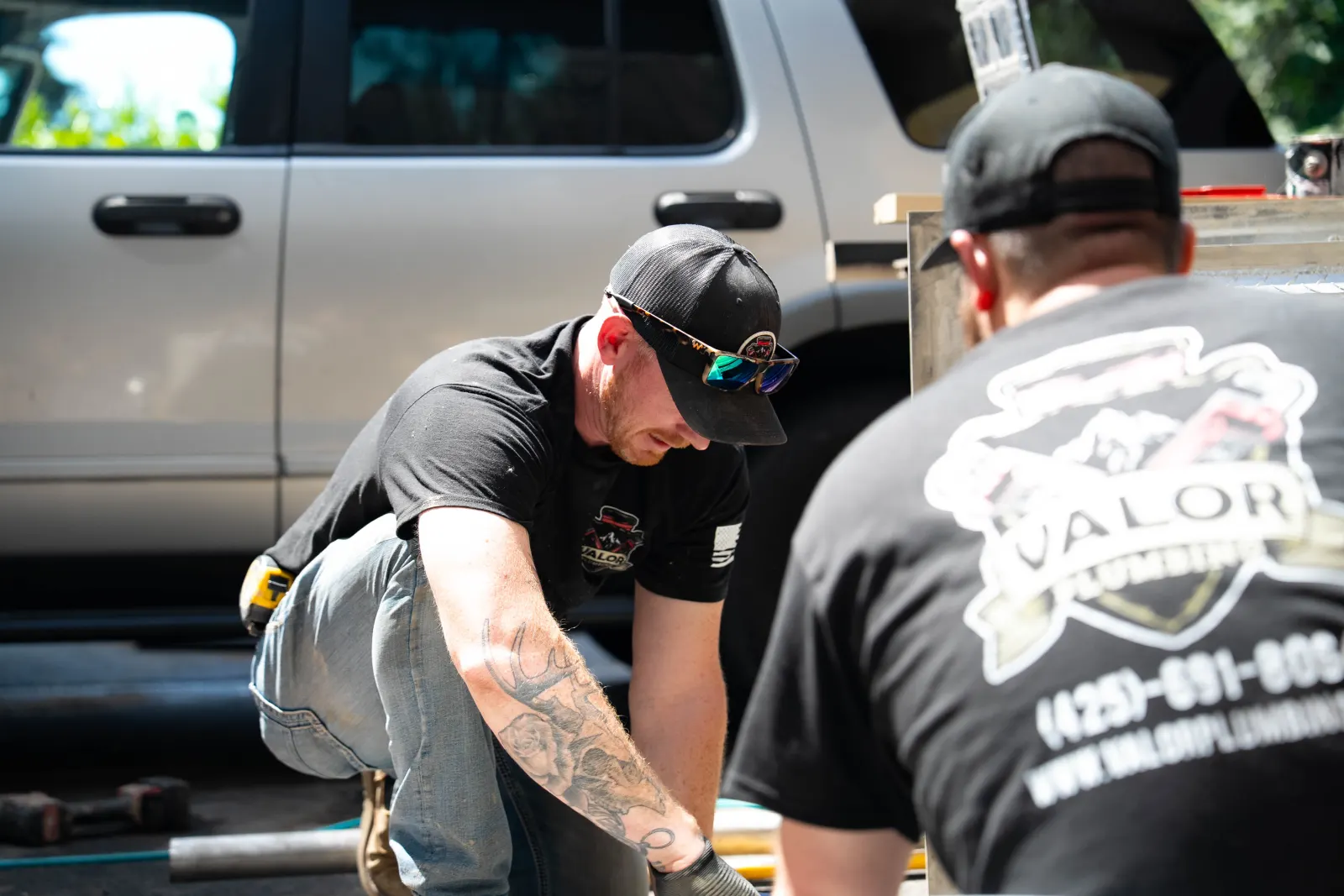 Valor Plumbing plumber working on a pipe next to a crew member in a Valor Plumbing shirt