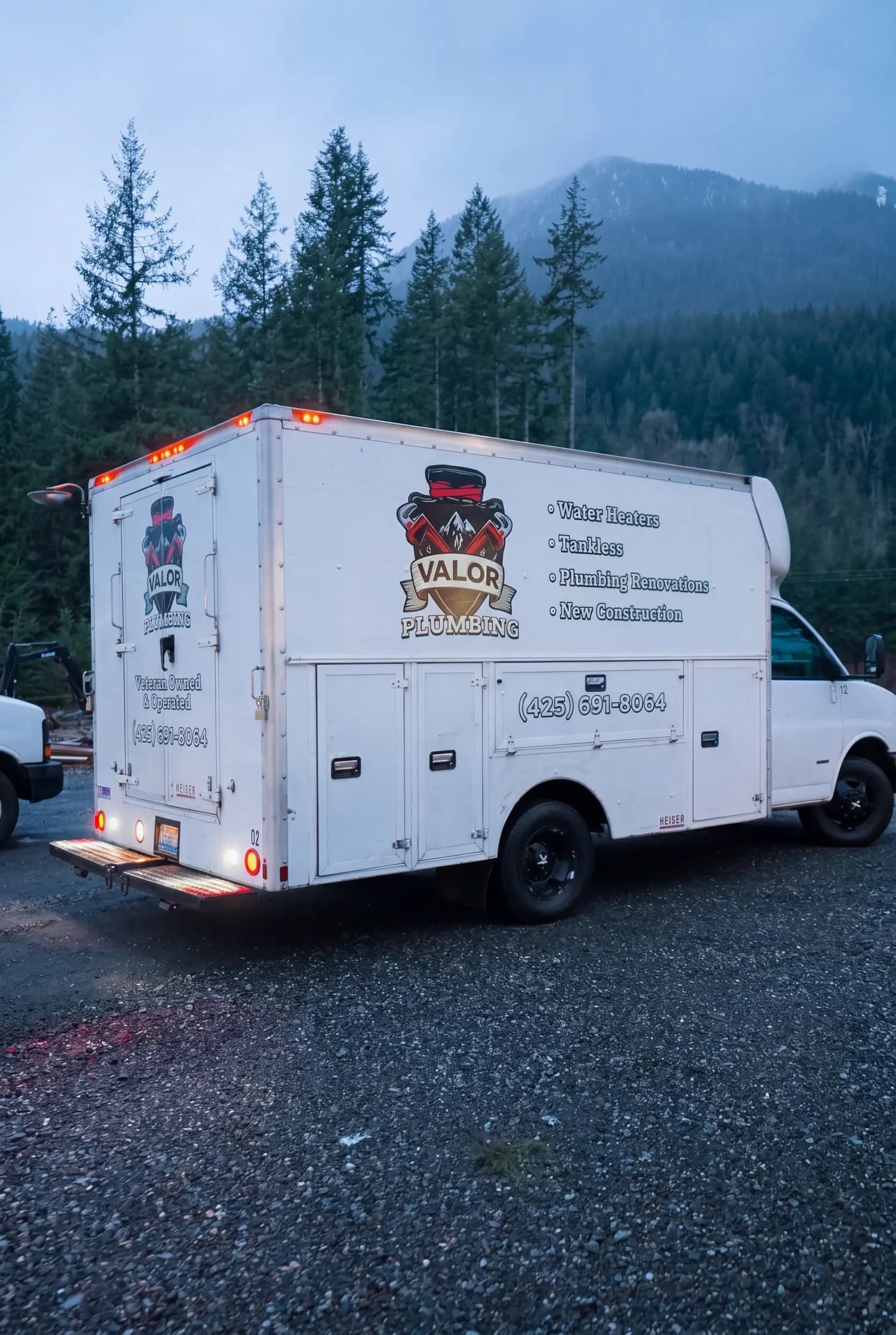 Valor Plumbing box truck parked at a gravel job site below forested mountains